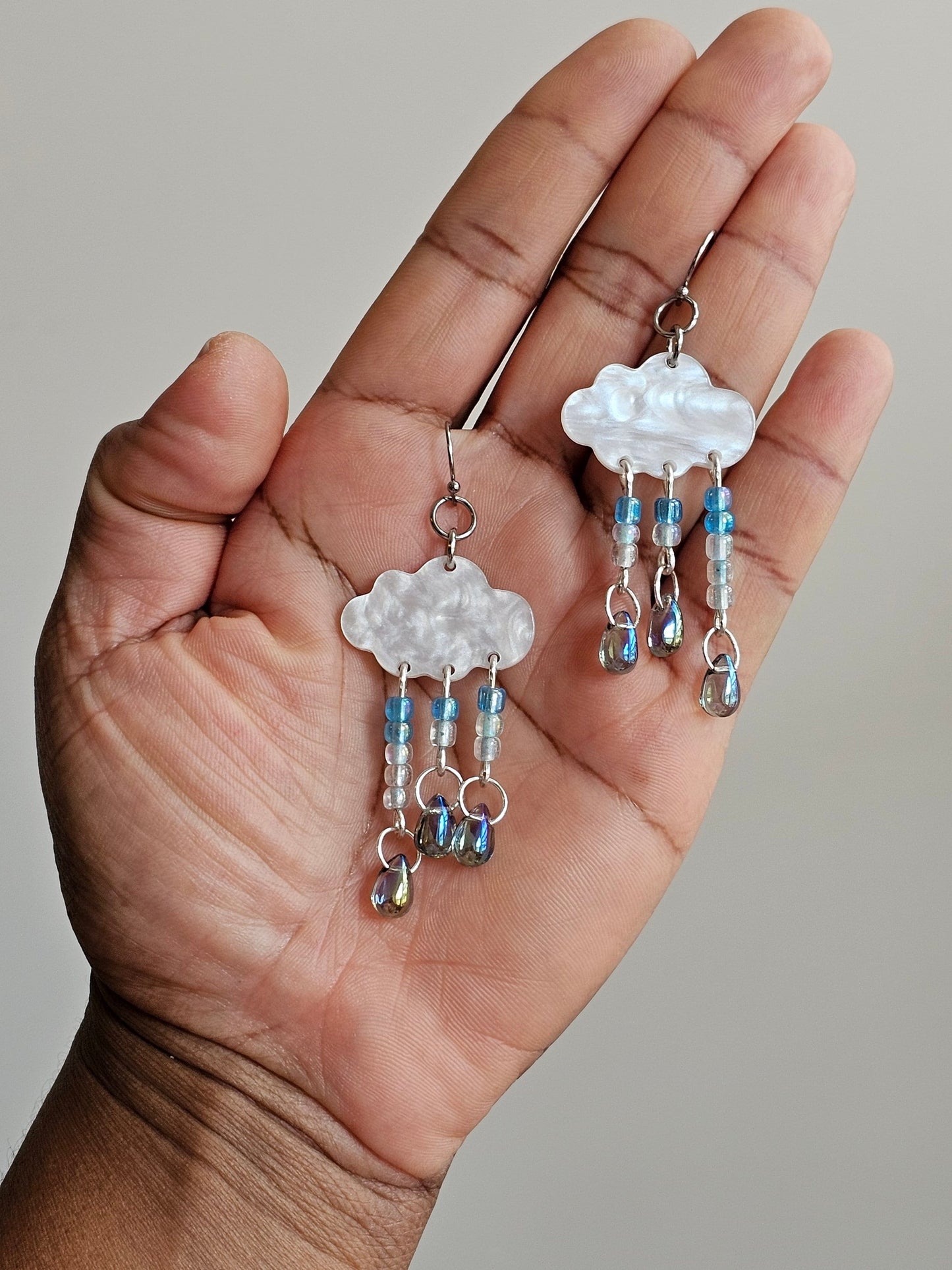 White and blue hypoallergenic earrings shaped like a cloud with rain droplets.