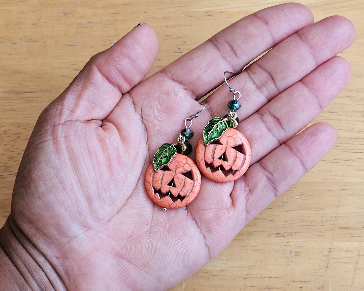 a hand holding a pair of earrings with carved pumpkins