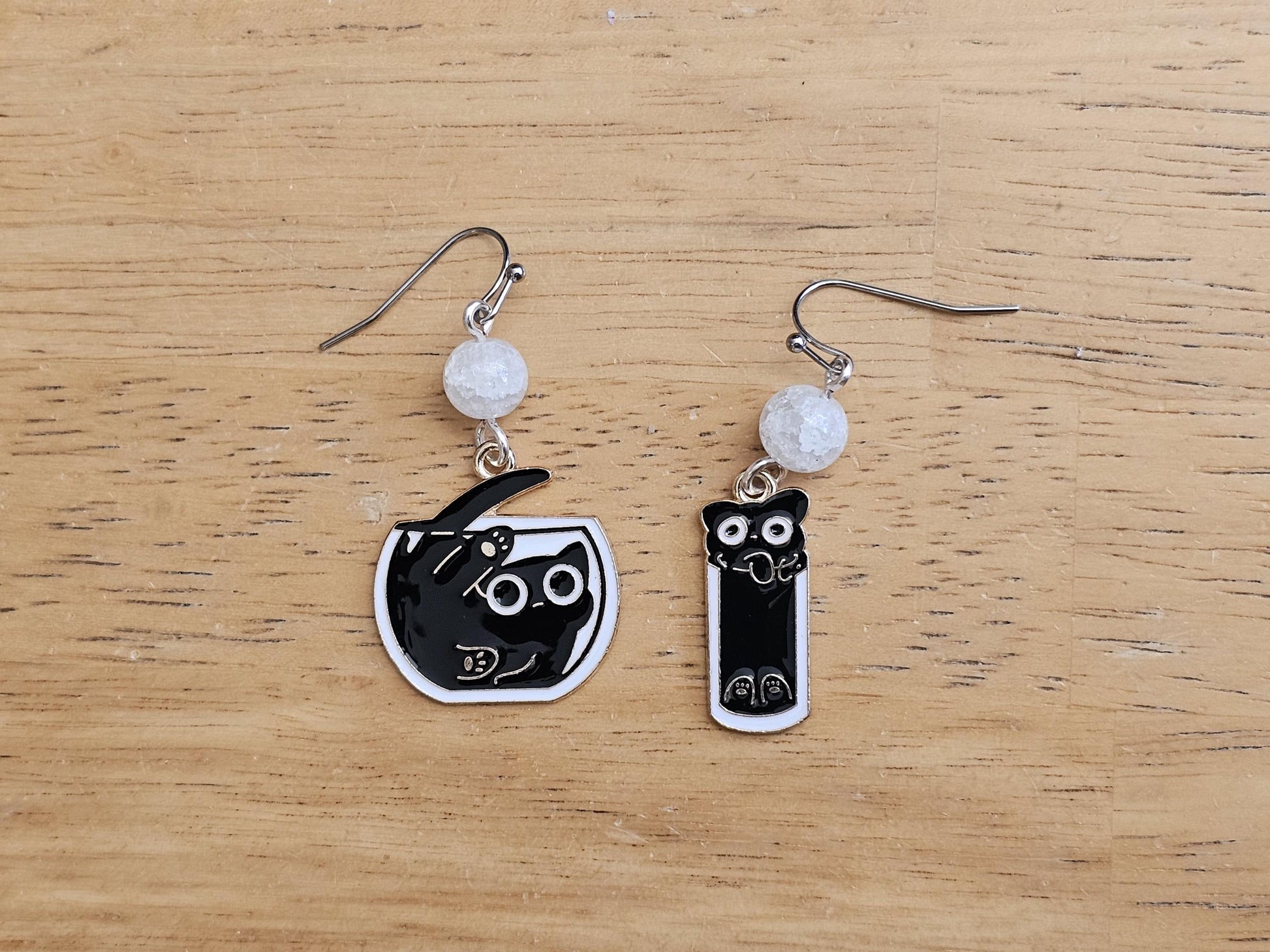 a pair of black and white cat earrings on a wooden table