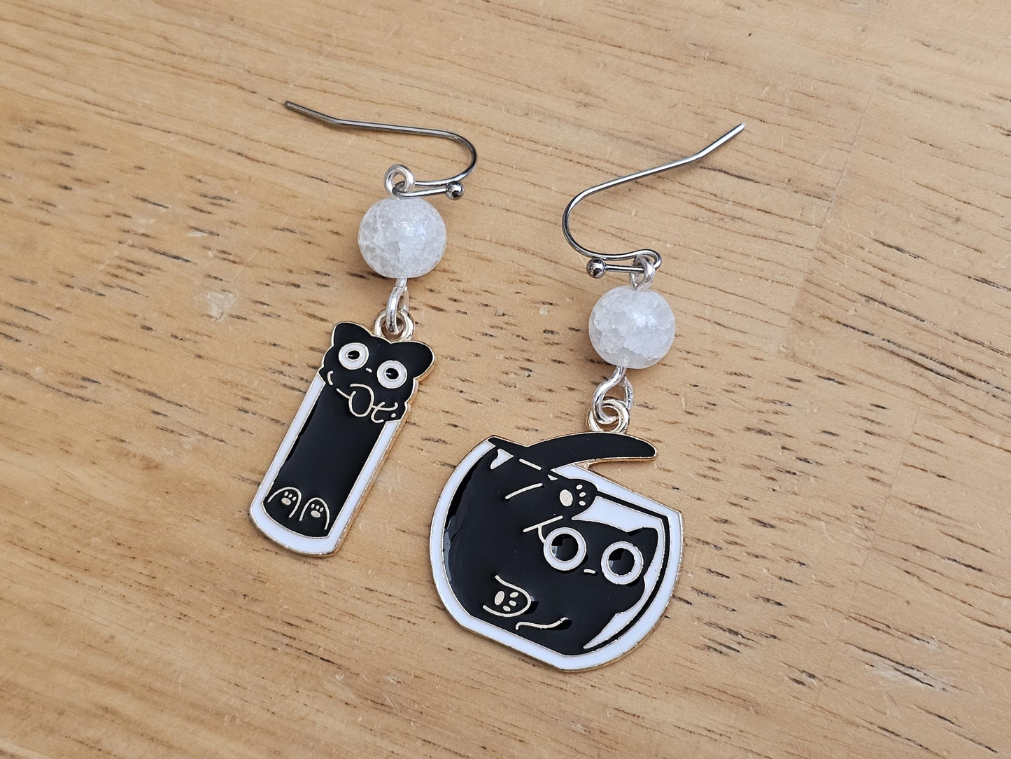 a pair of black and white cat earrings on a wooden table