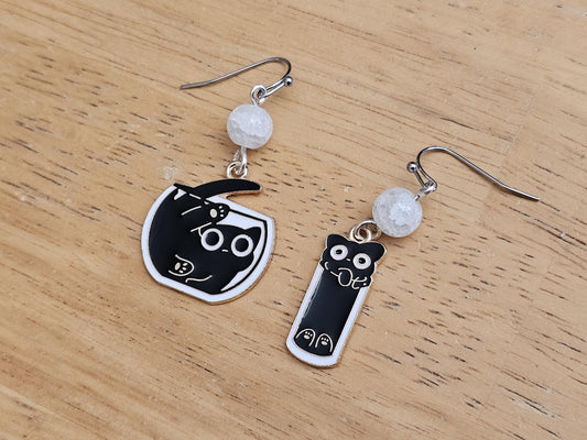 a pair of black and white cat earrings on a wooden table