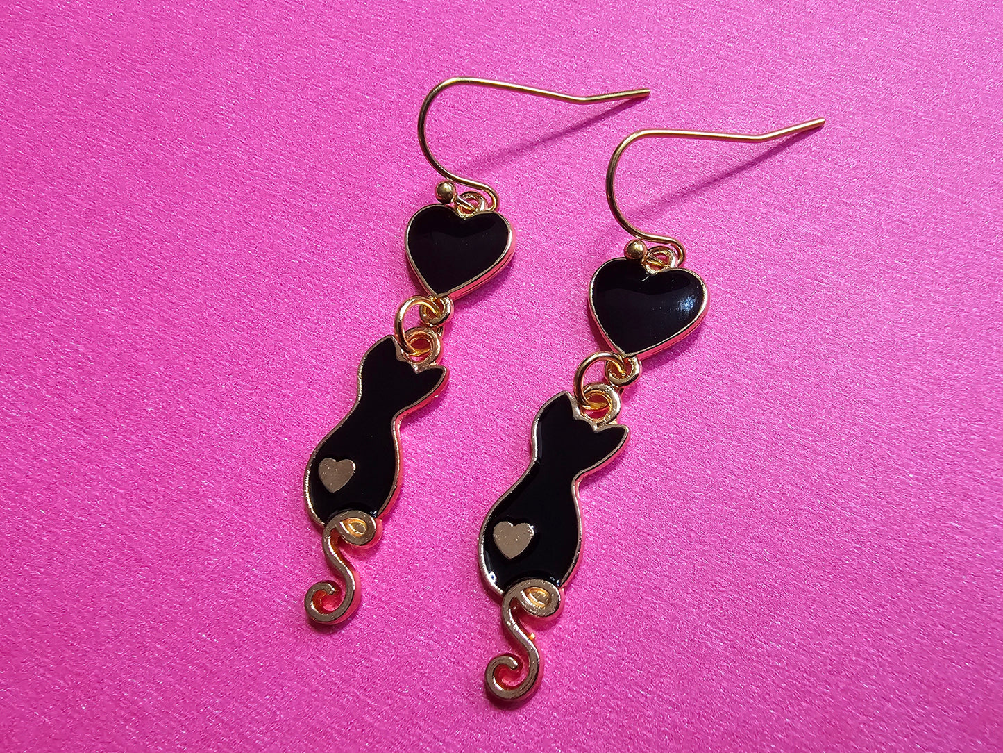 a pair of black and gold earrings on a pink background