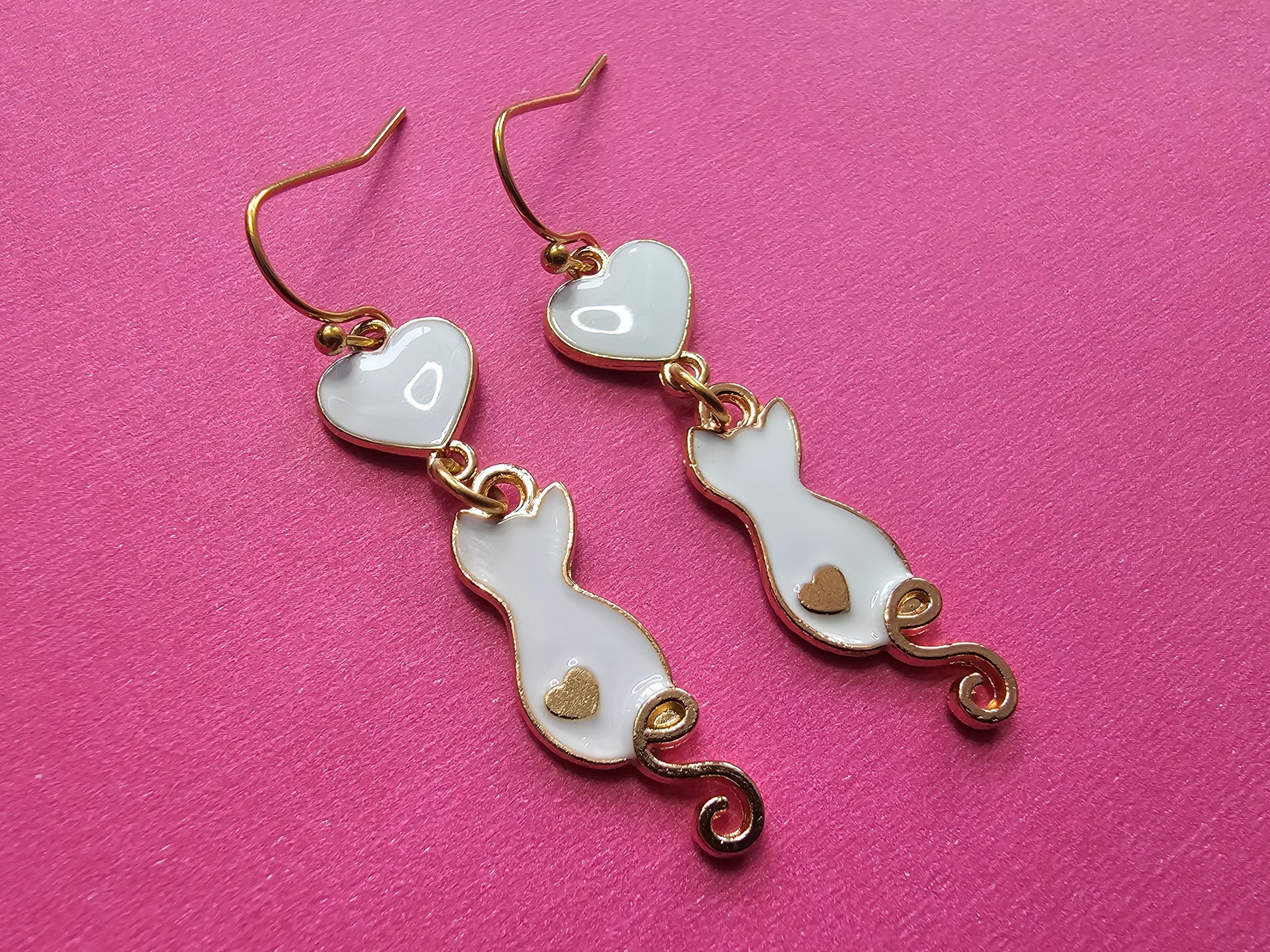 a pair of heart shaped earrings on a pink surface