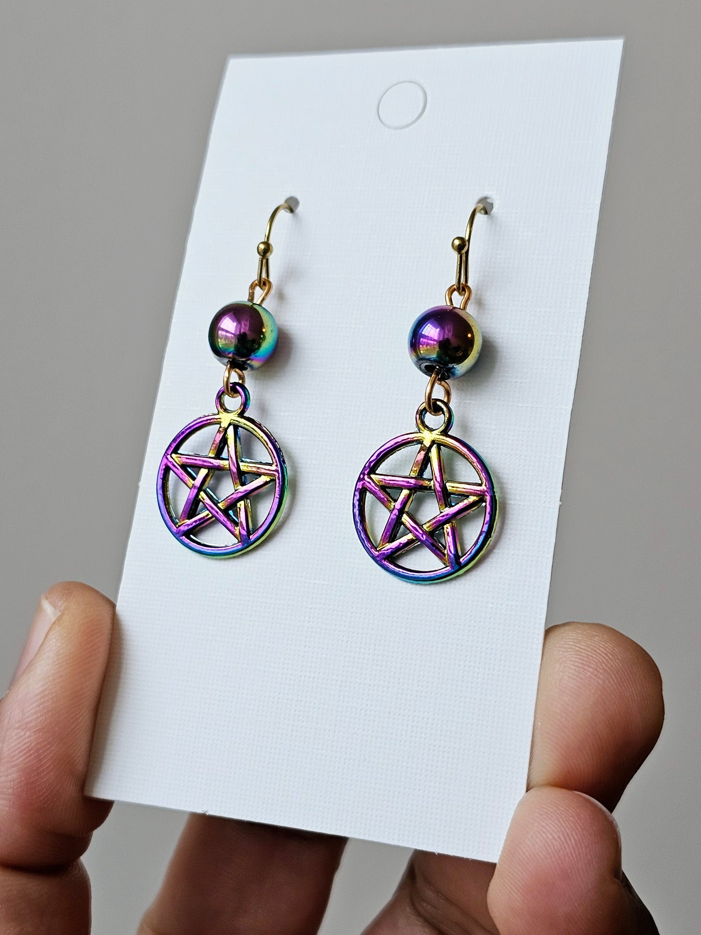 a hand holding a pair of earrings with a pentagramil on it